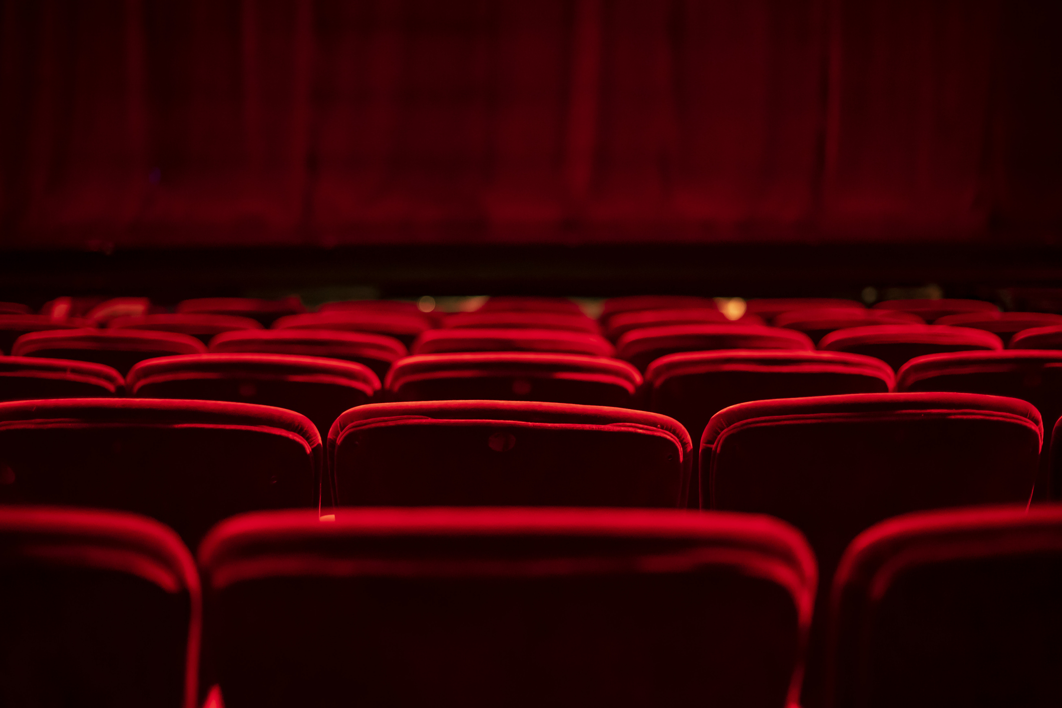 Kinosaal mit roten Sesseln und rotem Vorhang von hinten. 