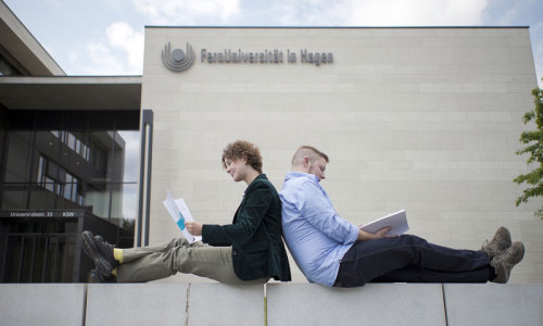 Zwei Studierende sitzend vor dem Gebäude der FernUniversität in Hagen